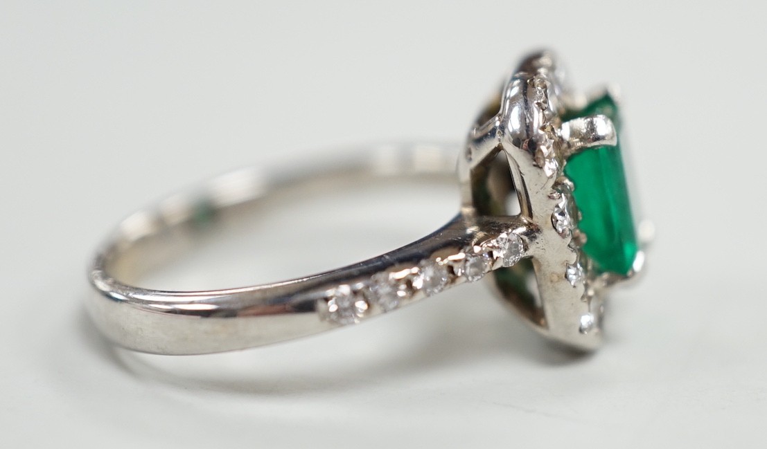 A modern 750 white metal, emerald and diamond set octagonal cluster ring, with diamond set shoulders, size J, gross weight 4.9 grams.